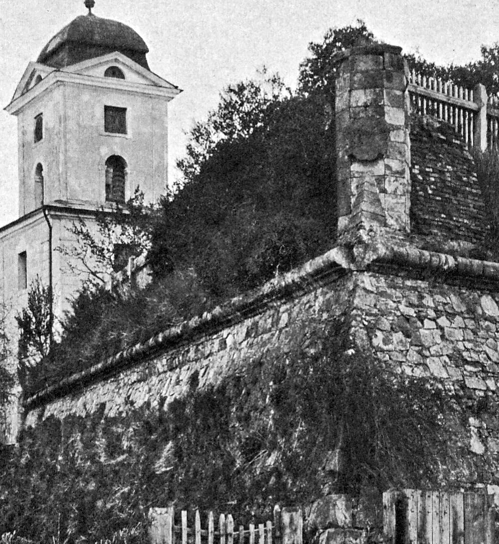 Narożnik bastionu zamku w Rzeszowie z kamiennym licem i zaokrągloną koroną muru, w głębi wieża przykryta niską kopułą z latarnią