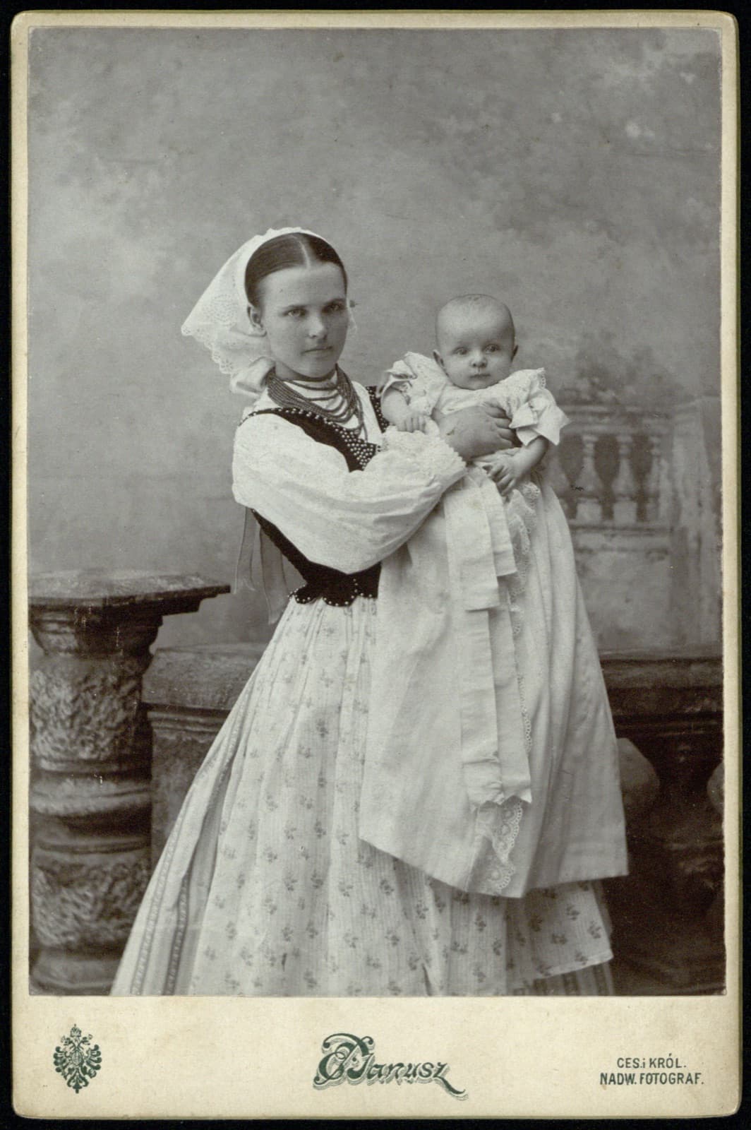 Edward Janusz (Rzeszów) – portret młodej kobiety w stroju rzeszowskim z niemowlęciem (mężatka; wg przekazu rodzinnego – babcia rodziny), fotografia gabinetowa [strój ludowy / etnografia]